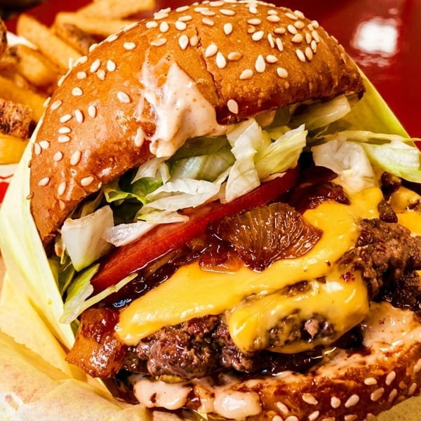 Cheeseburger with lettuce, tomato, caramelized onions, and special sauce, next to a basket of fries.