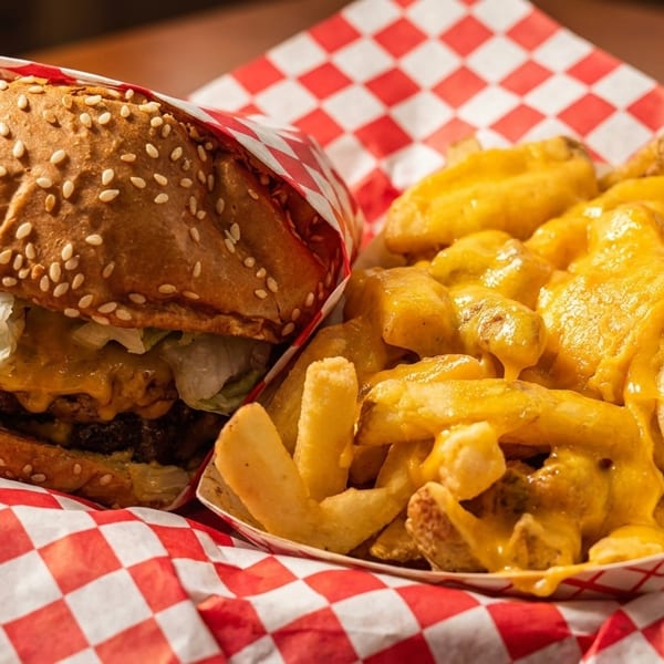 Cheeseburger wrapped in red and white checkered paper next to a container of cheese fries.