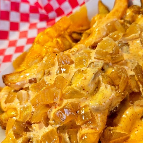 Golden french fries topped with creamy sauce and caramelized onions in a red and white checkered basket.